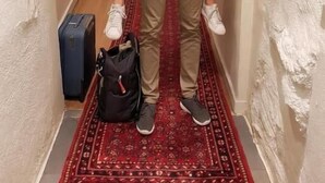 A hallway with a red patterned carpet, a suitcase, and a person carrying another person.
