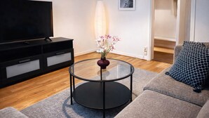 A modern living room with a glass coffee table, a sofa, a TV, a lamp, and a framed picture on the wall.