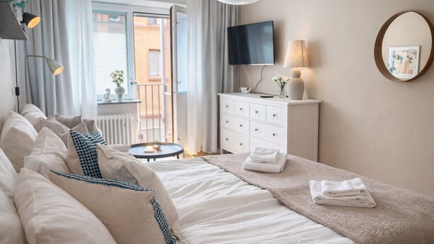 A hotel room with a large bed, a small round table, a dresser, and a TV on the wall.