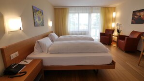 A hotel room with a large bed, a desk with a phone, two chairs, and a window with curtains.
