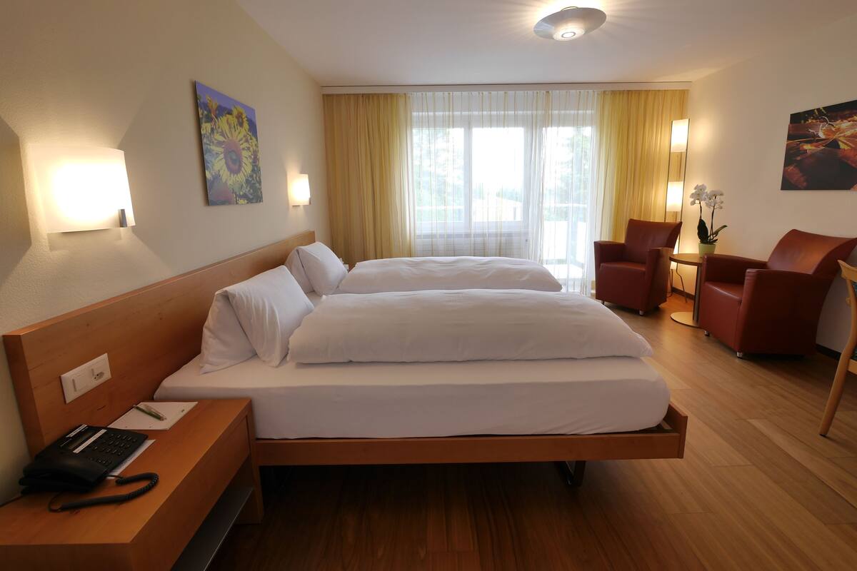 A hotel room with a large bed, a desk with a phone, two chairs, and a window with curtains.