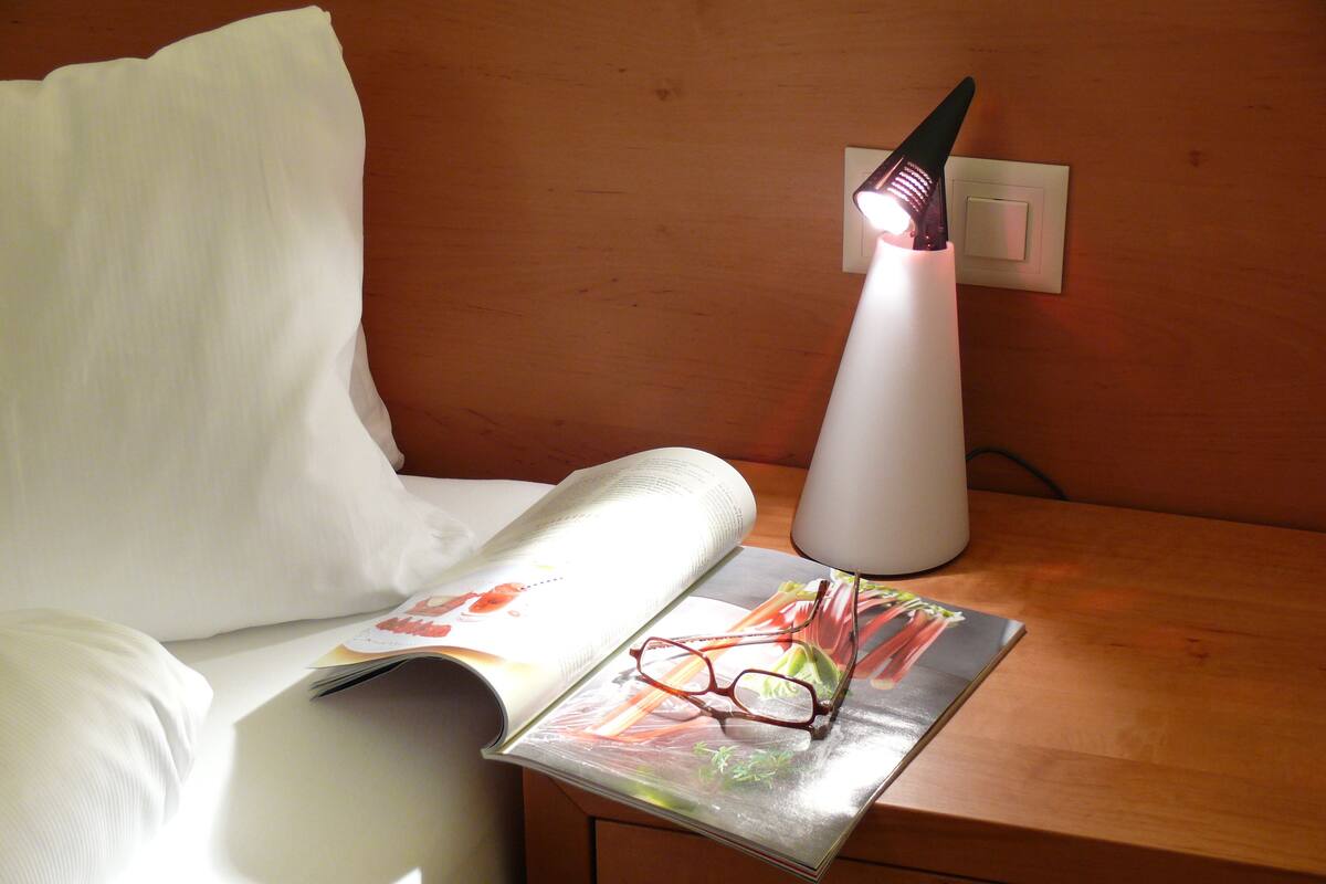 A neatly made bed with a white pillow and a magazine with glasses on it.