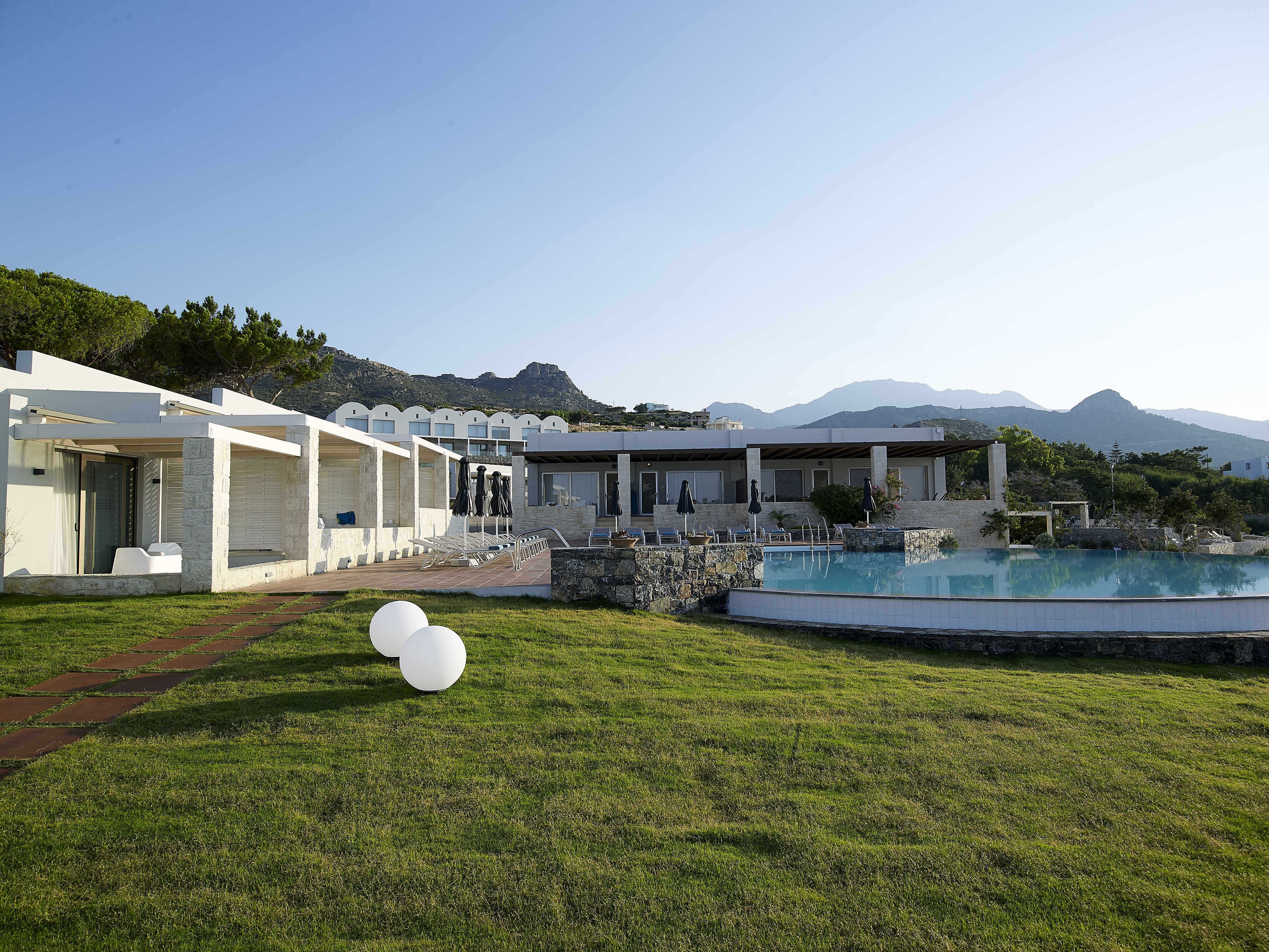 A modern resort with a swimming pool, outdoor seating, and a view of mountains.