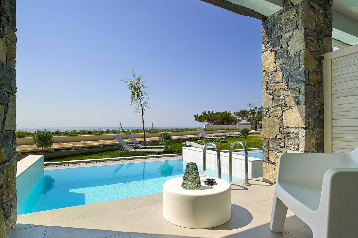 Un espace piscine offrant une vue dégagée sur la mer, avec des chaises longues et un mur en pierre.