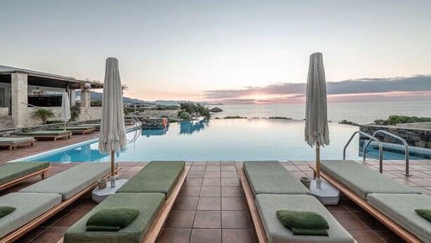 Ein Poolbereich mit Liegestühlen und Sonnenschirmen, mit Blick auf ein Gewässer und einen Sonnenuntergang.