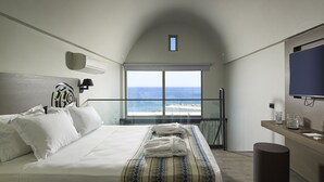 Ein Hotelzimmer mit einem großen Bett, Meerblick, einem Fernseher und einem kleinen Tisch mit Glas und Tasse.