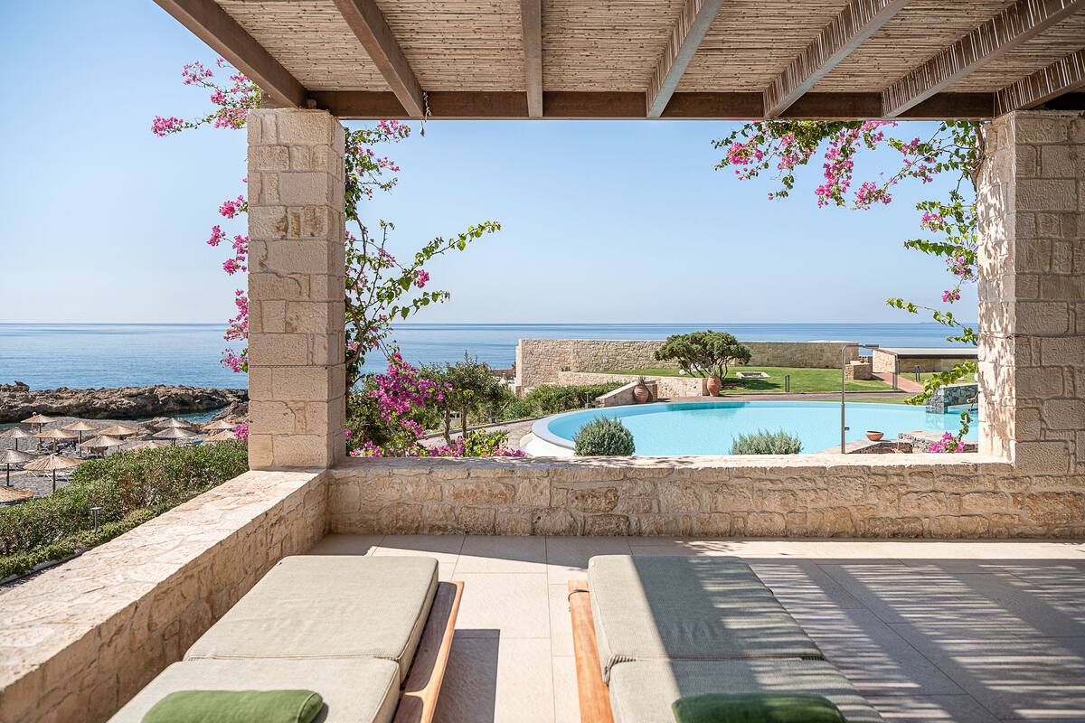 Un espace aménagé au bord de la piscine, avec des chaises longues, une vue sur la mer et un mur en pierre.