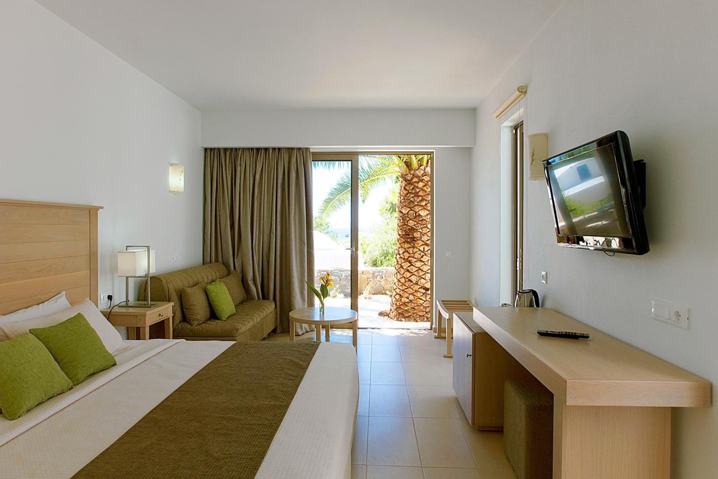 A hotel room with a bed, a sofa, a desk, a TV, and a view of the outdoors.