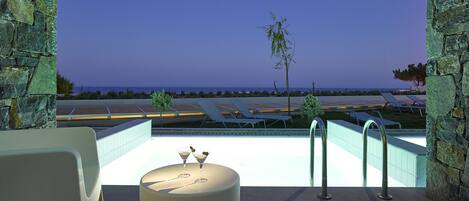 A rooftop pool area with lounge chairs and a view of the ocean at dusk.