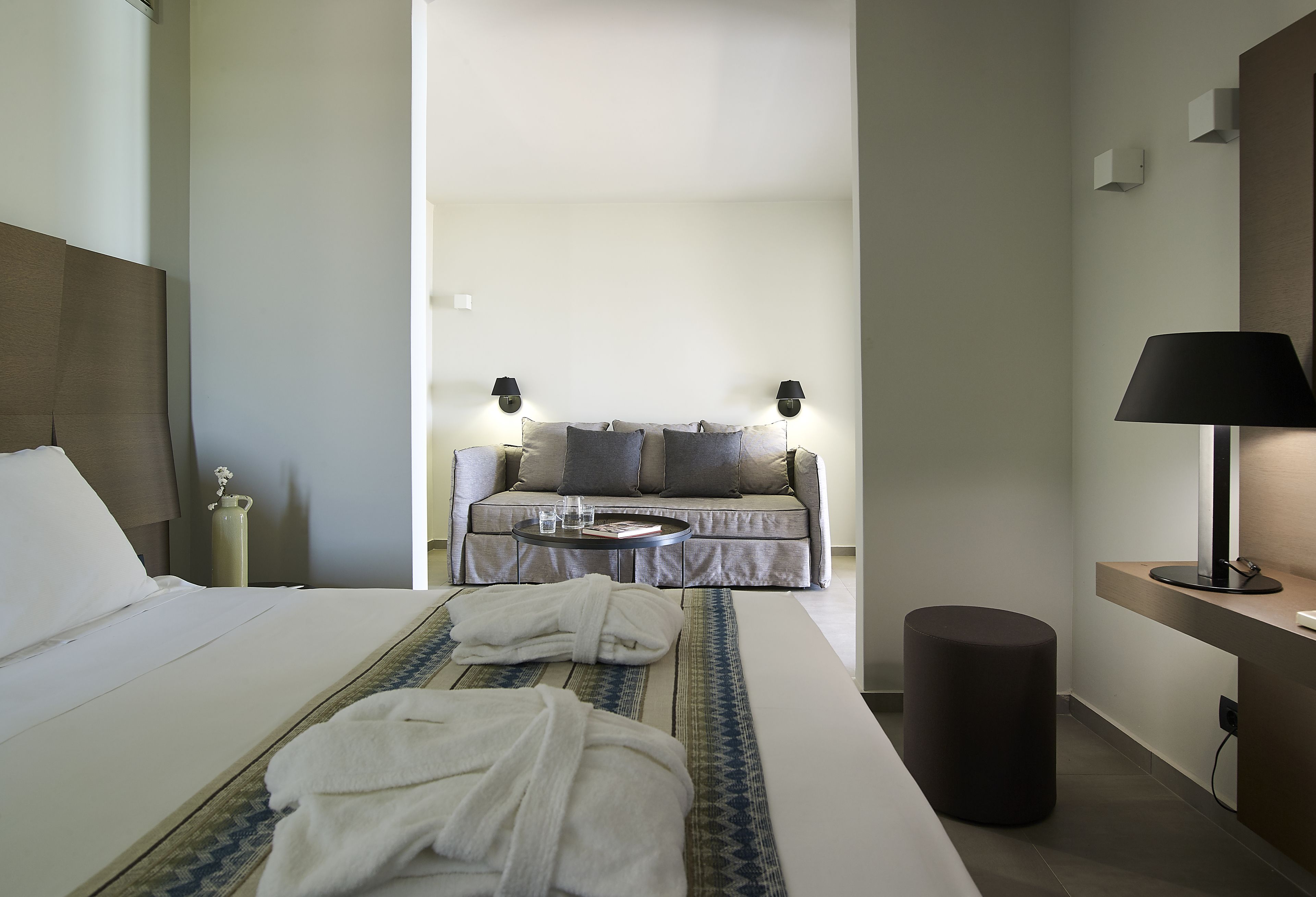 A hotel room with a bed, a bedside table, a lamp, a sofa, and a coffee table.