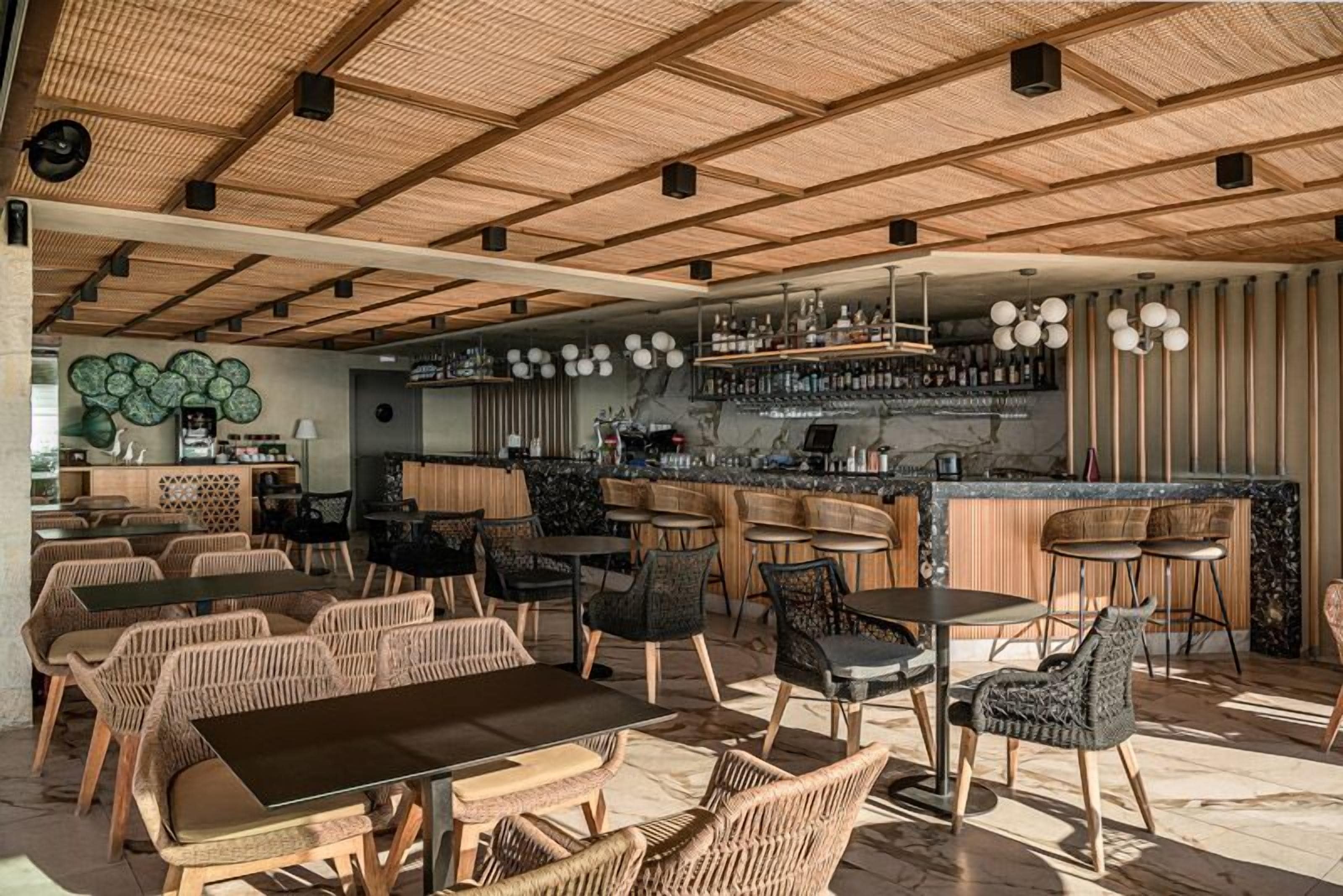 A modern bar area with wicker furniture, a bar counter, and a ceiling with wooden beams.
