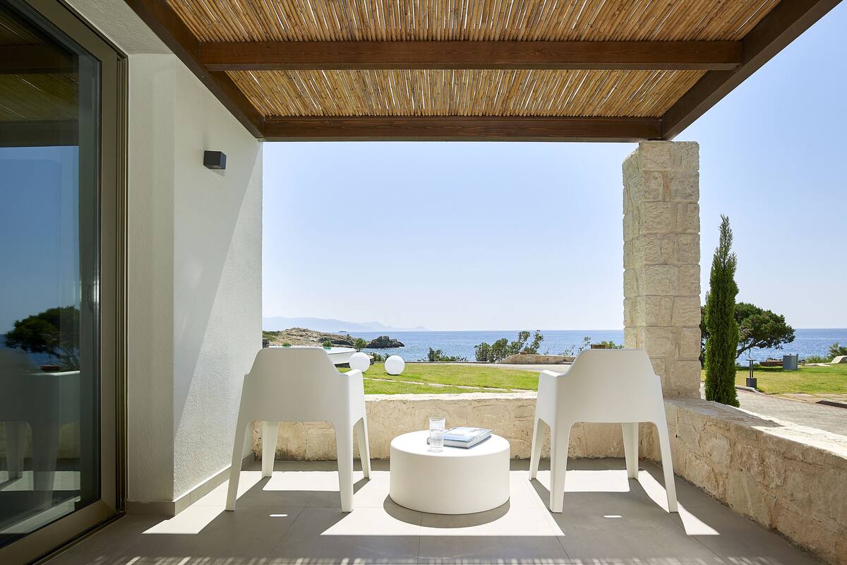 Un espace extérieur abrité, aménagé avec deux chaises blanches et une table ronde, offrant une vue sur un paysage côtier.