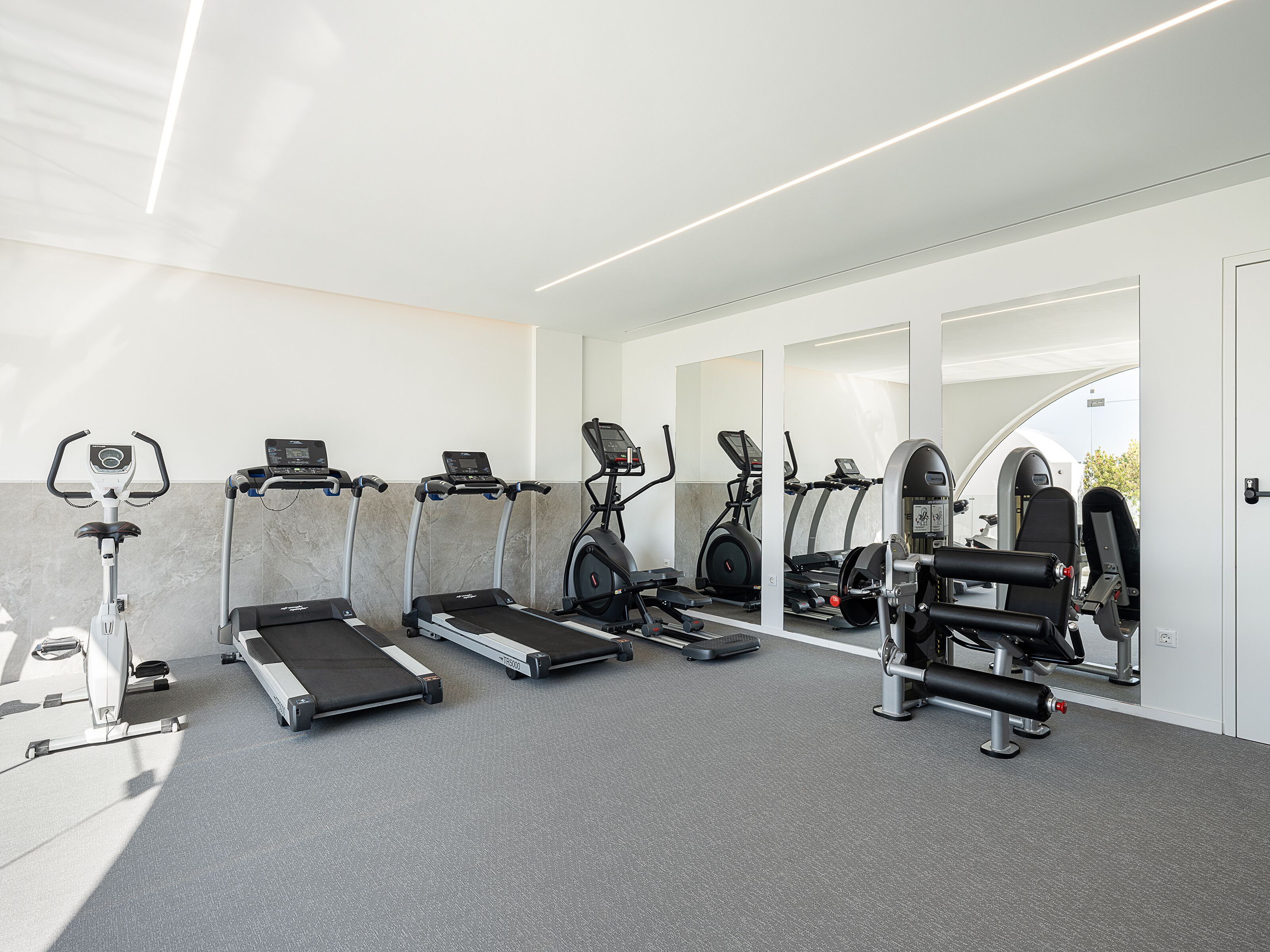 Academia moderna com diversos equipamentos de cardio, aparelhos de musculação e um interior limpo e bem iluminado.