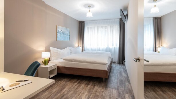 A hotel room with a bed, bedside table, lamp, chair, and a painting on the wall. - Hotel Birsighof (Basel)