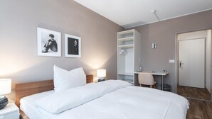 A hotel room with a bed, bedside table, lamp, wall-mounted pictures, a wardrobe, a mirror, and a door. - Hotel Birsighof (Basel)