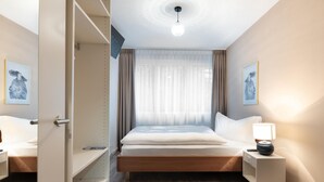 A hotel room with a bed, bedside tables, a wardrobe, and artwork on the walls. - Hotel Birsighof (Basel)