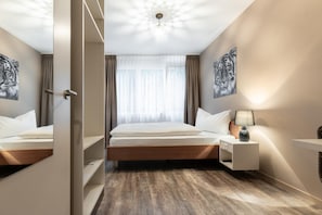 Habitación de hotel con piso de madera, una cama con ropa blanca, una mesita de noche con lámpara y dos obras de arte en la pared con temática de tigres.