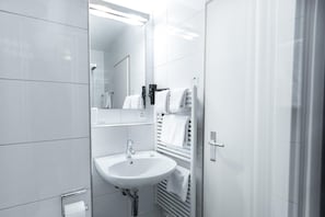 Un baño moderno con lavabo blanco, espejo, toallero y secatoallas.