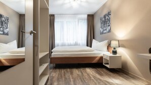 A hotel room with a wooden floor, a bed with white linens, a nightstand with a lamp, and two tiger-themed wall art pieces. - Hotel Birsighof (Basel)