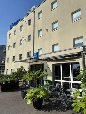 Een hotelgevel met een bord waarop 'ibis budget' staat, terrasmeubels en potplanten.