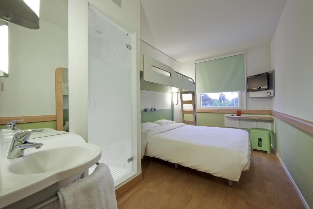 A hotel room with a bed, a bathroom with a sink and mirror, a window with a view, and a TV mounted on the wall.