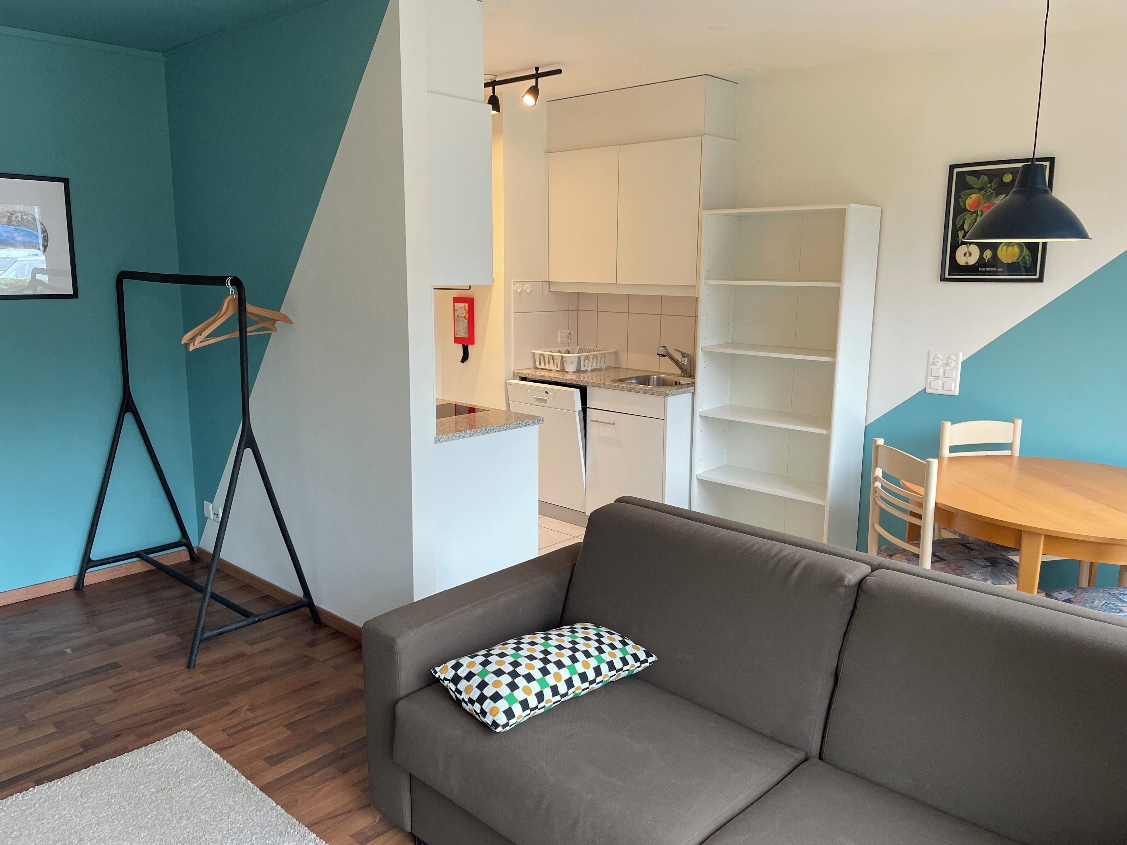 A modern living room with a sofa, a dining table, and a kitchen area.