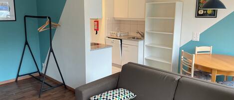A modern living room with a sofa, a dining table, and a kitchen area.