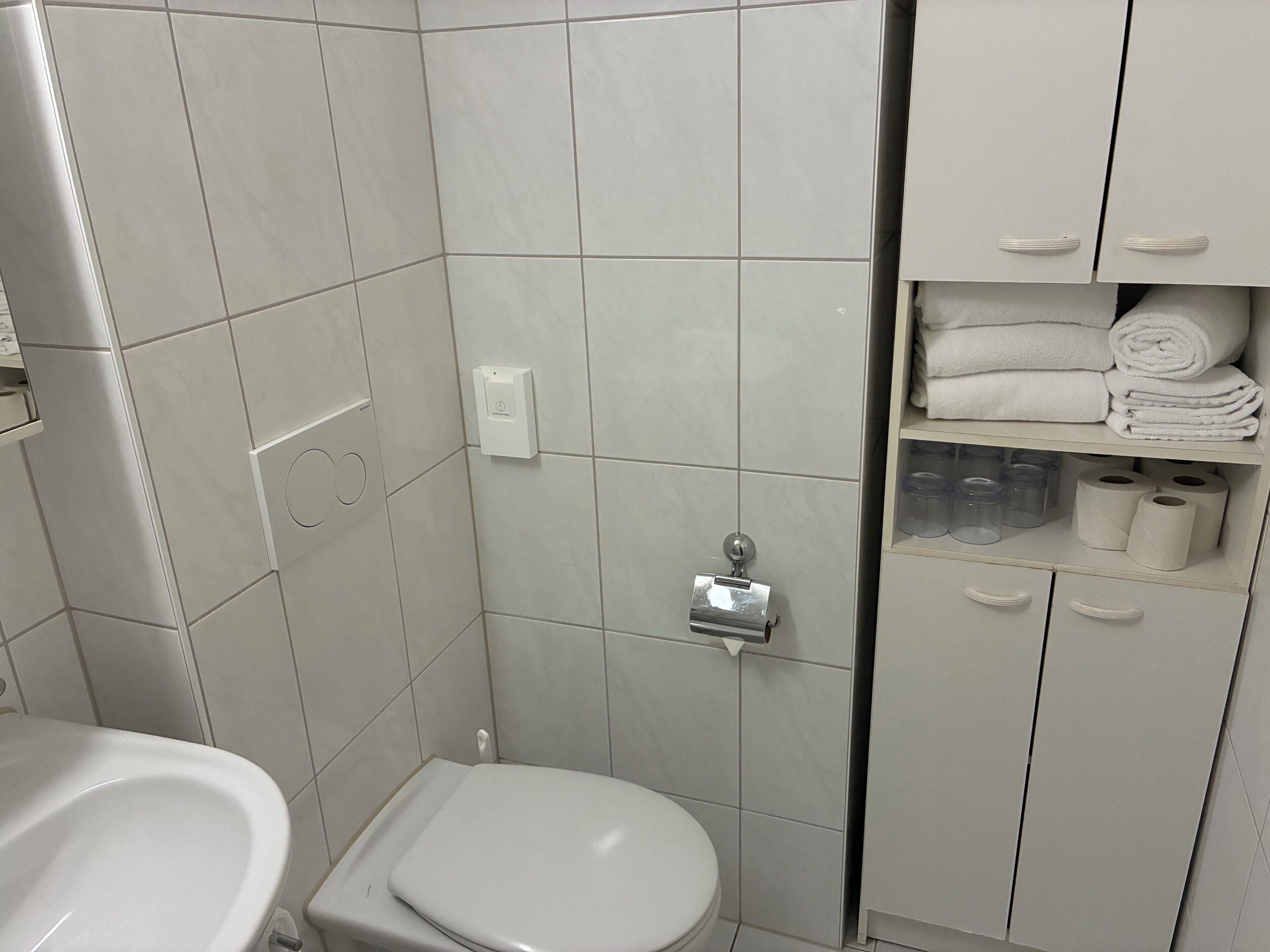 Un baño con inodoro, lavamanos y un mueble con toallas y artículos de aseo.