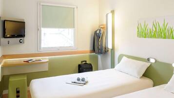 Een hotelkamer met twee bedden, een bureau met een televisie, een raam en een schilderij van gras.