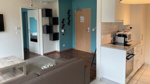 A modern living room with a sofa, a coffee table, a kitchen with a microwave, and a teal accent wall.