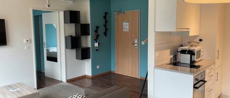 Una sala de estar moderna con sofá, una mesa de centro, una cocina con microondas y una pared de acento color aguamarina.