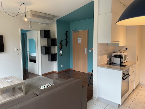 A modern living room with a sofa, a coffee table, a kitchen with a microwave, and a teal accent wall.