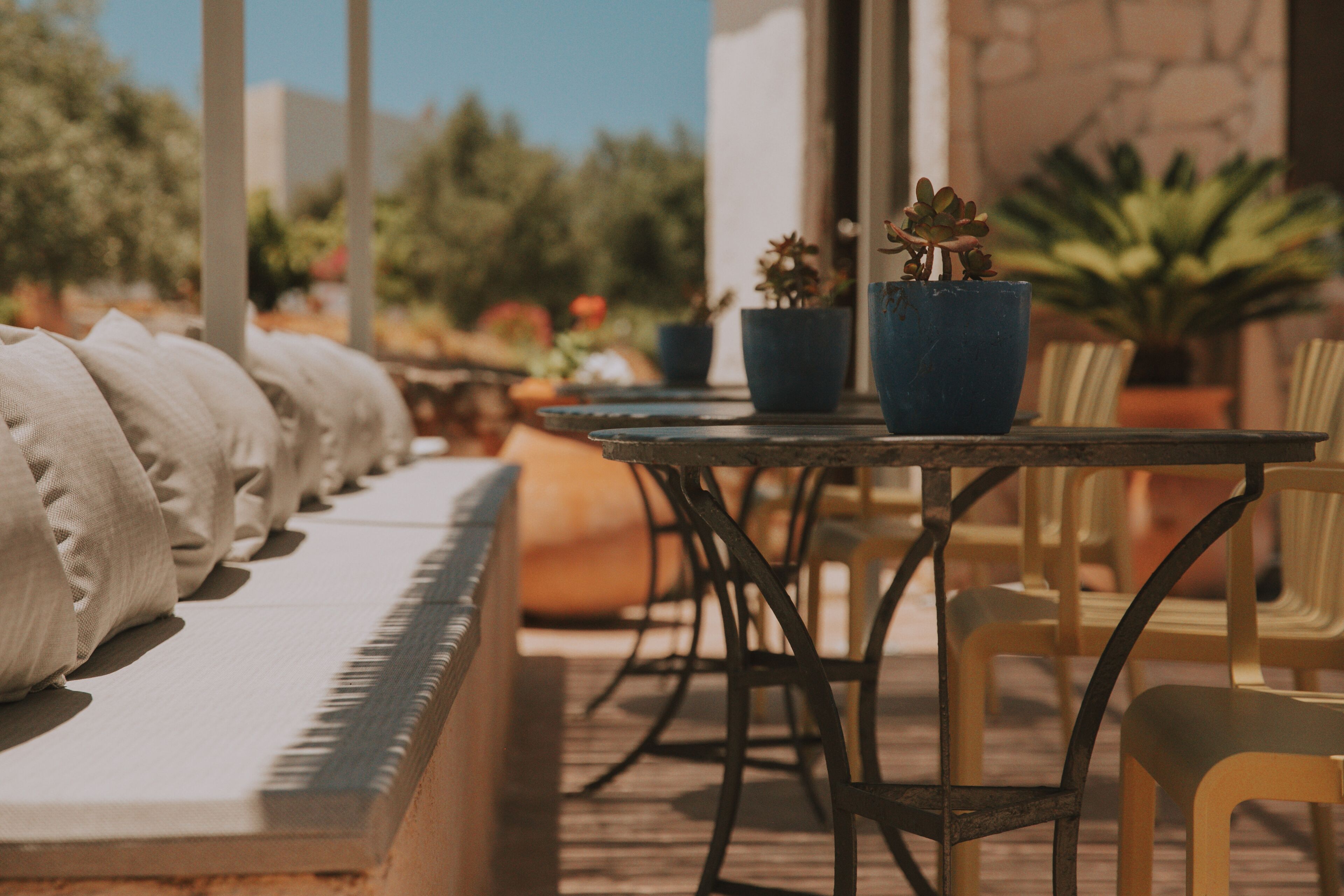 Un espace extérieur ensoleillé, aménagé avec un long banc, une table ronde et des chaises.