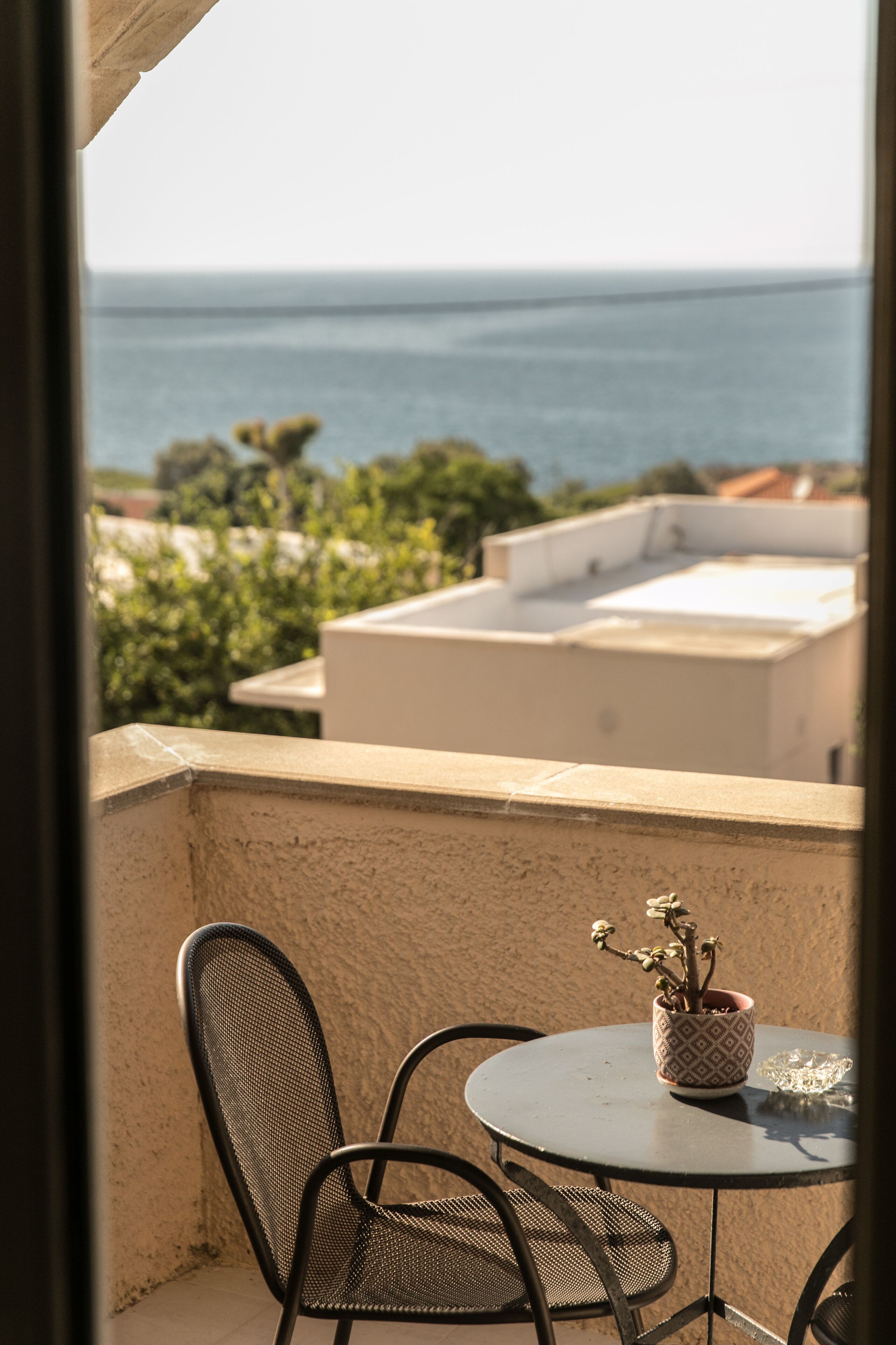 A balcony with a round table and two chairs, overlooking a body of water and buildings.