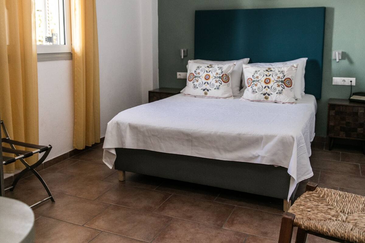 A bedroom with a bed, a chair, a nightstand, and a wall-mounted air conditioner.