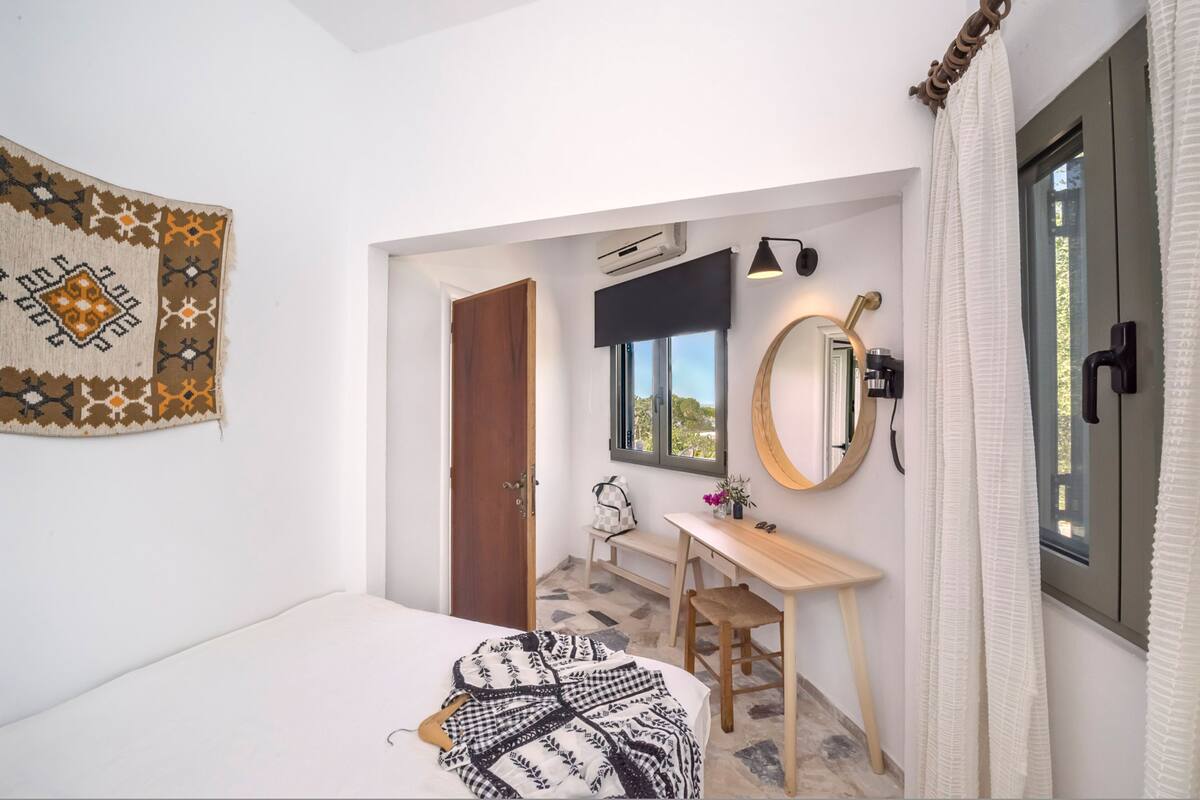 A compact room with a bed, a desk, a mirror, and a window.