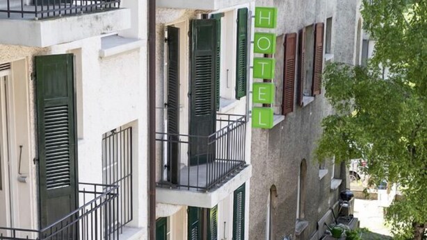 Un hotel con un letrero verde, mesas al aire libre y un pequeño jardín.