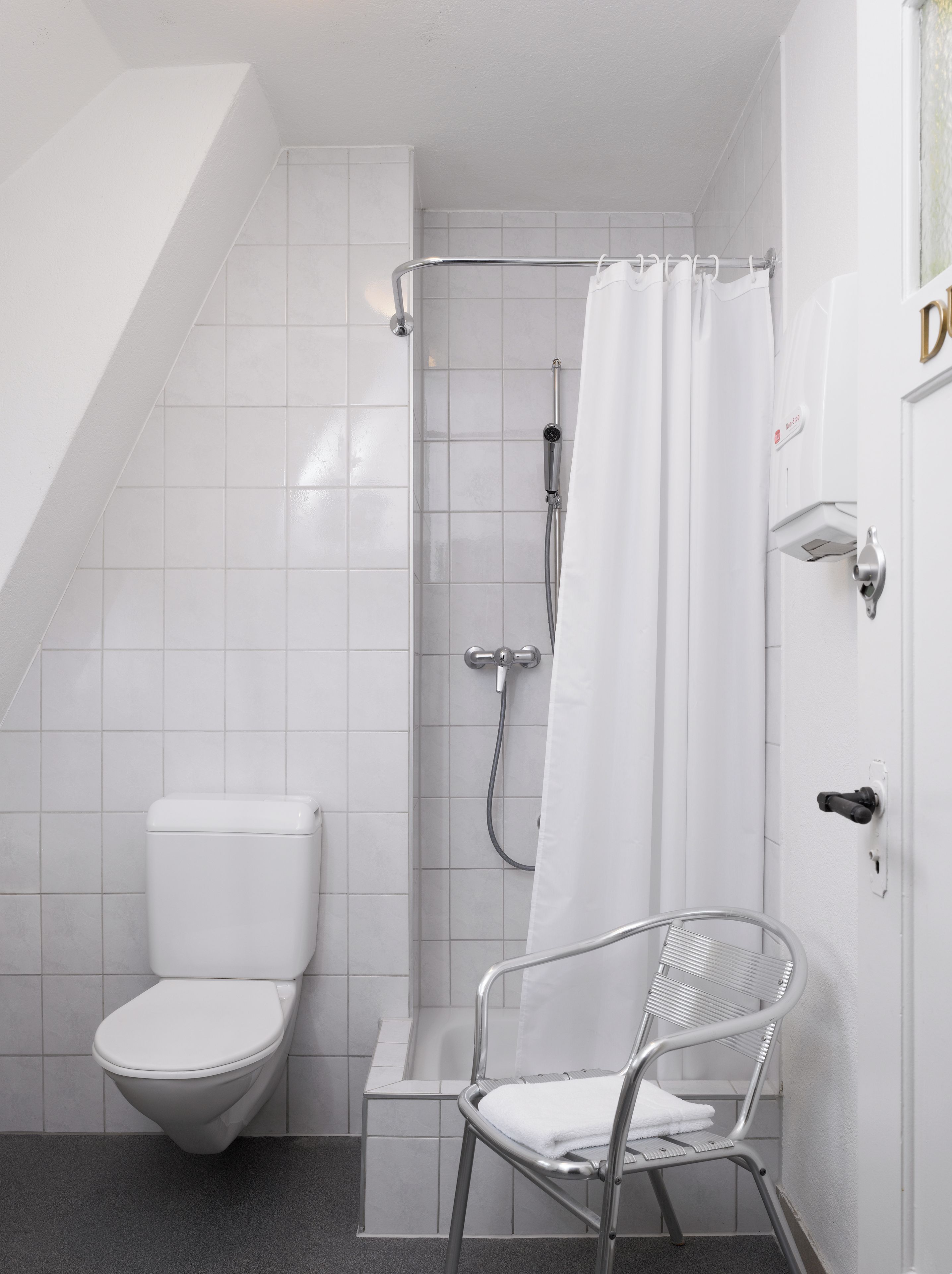 A modern bathroom with a shower, toilet, and a chair.