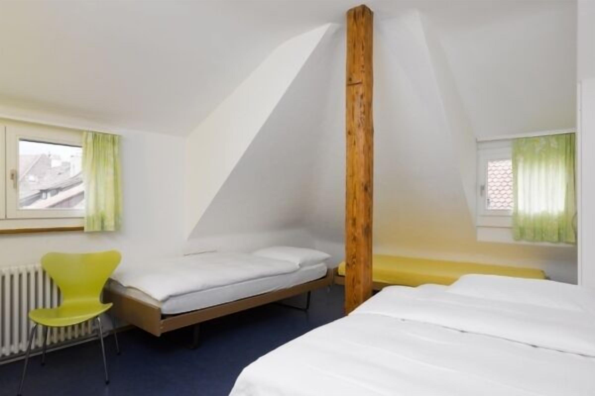 Une pièce avec un lit, une chaise, une fenêtre et un radiateur.