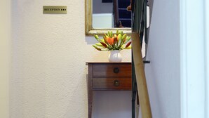 Un área de recepción con mostrador, un espejo y un florero con flores.