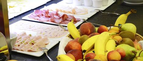 A buffet with various food items including sliced meats, fruits, and a basket of bananas and apples.
