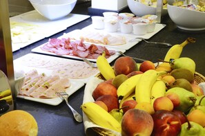 Un buffet proposant une variété d’aliments, notamment des viandes en tranches, des fruits, ainsi qu’un panier de bananes et de pommes.