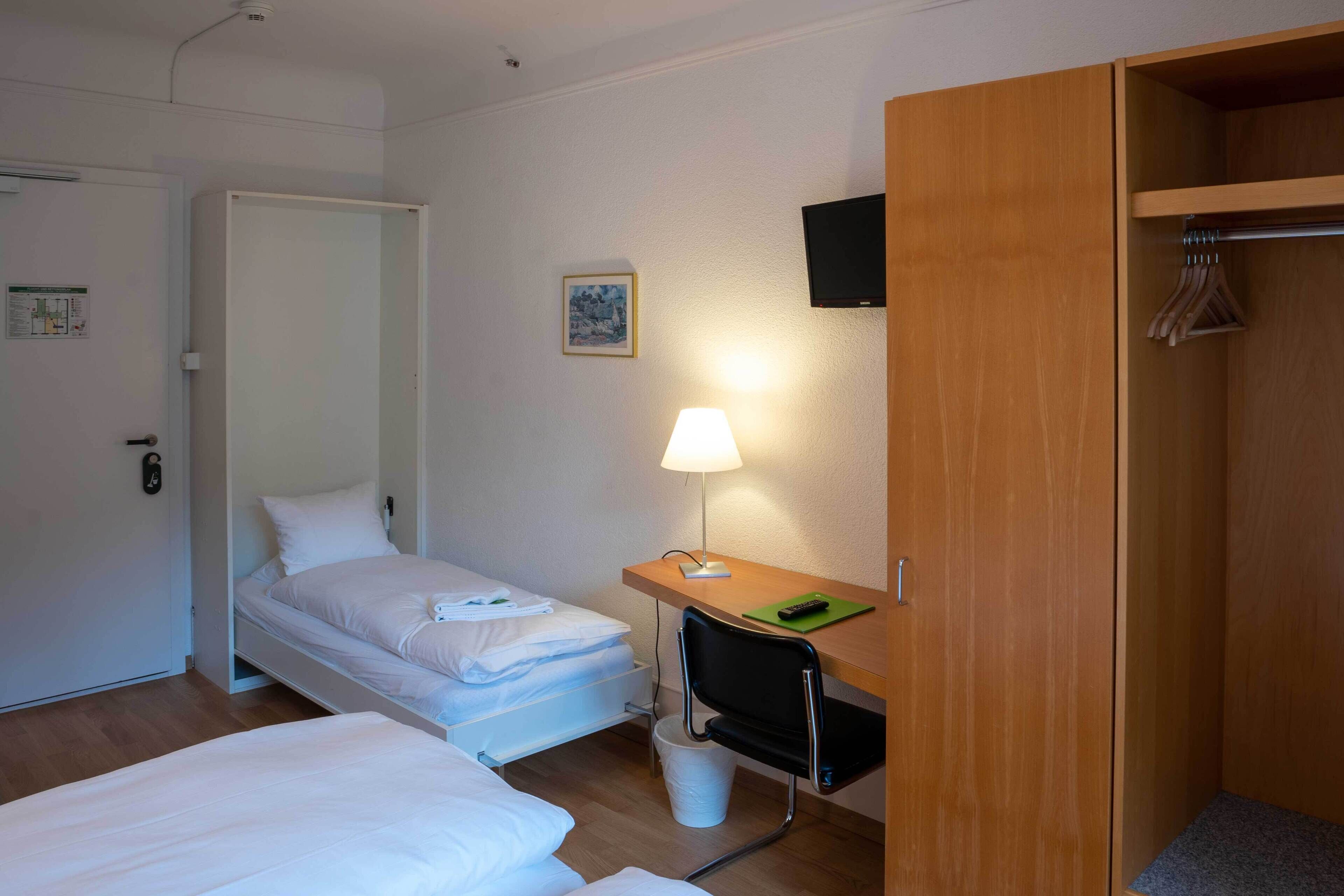 Une chambre d’hôtel avec deux lits, un bureau avec une lampe, une télévision et une armoire.