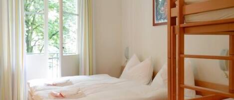 Una habitación con una cama, una cama litera de madera y una ventana con vistas a árboles.