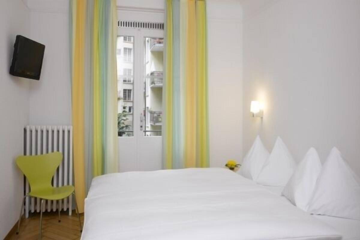 Ein Hotelzimmer mit einem Bett, einem Sessel, einem Heizkörper und einer Tür mit Blick auf Gebäude.