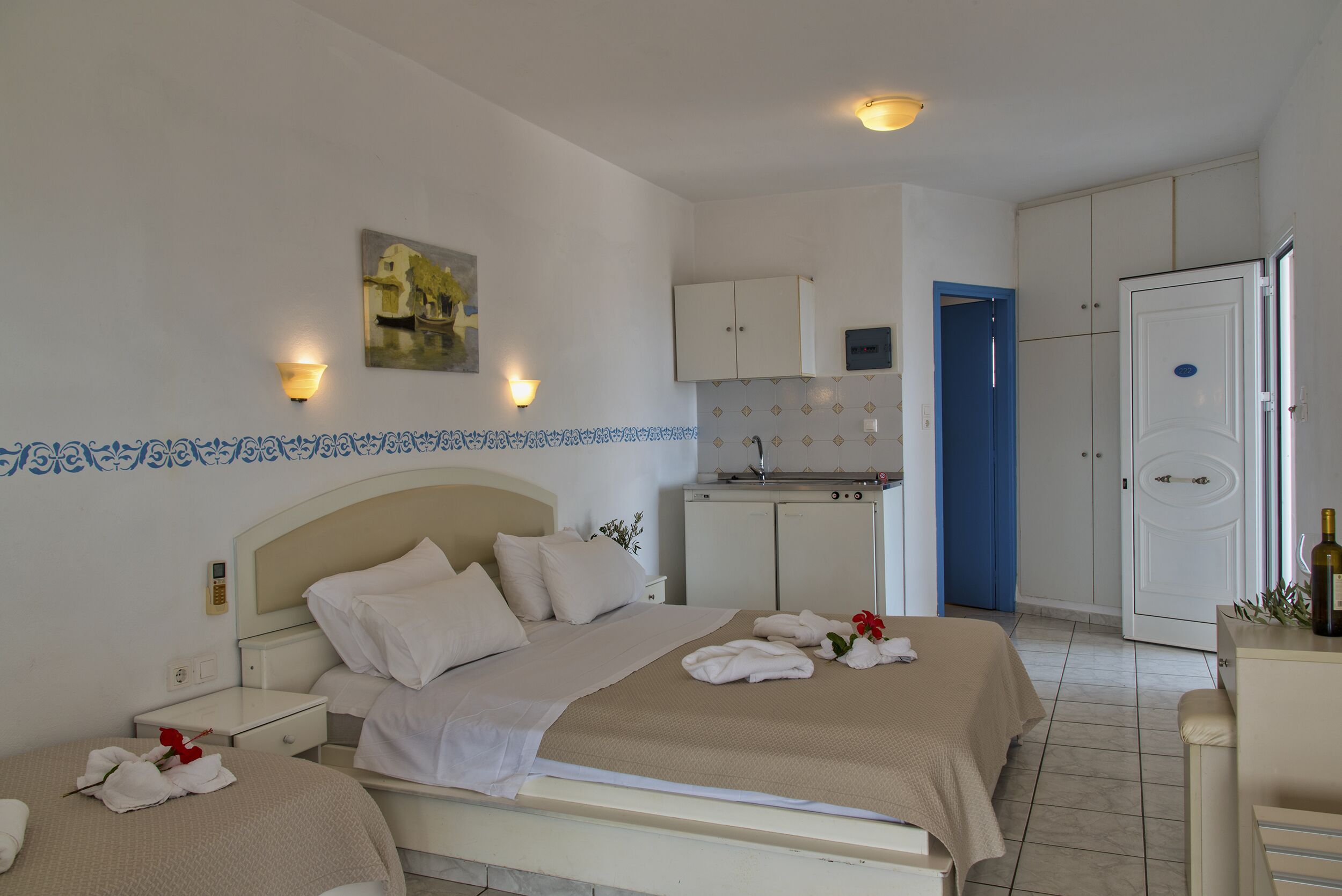 A hotel room with a bed, bedside tables, a small desk, a wardrobe, and a bathroom visible through an open door.