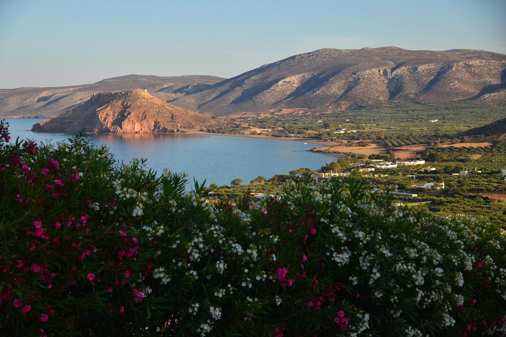 A coastal landscape with a prominent rocky hill, a body of water, and a village in the distance.