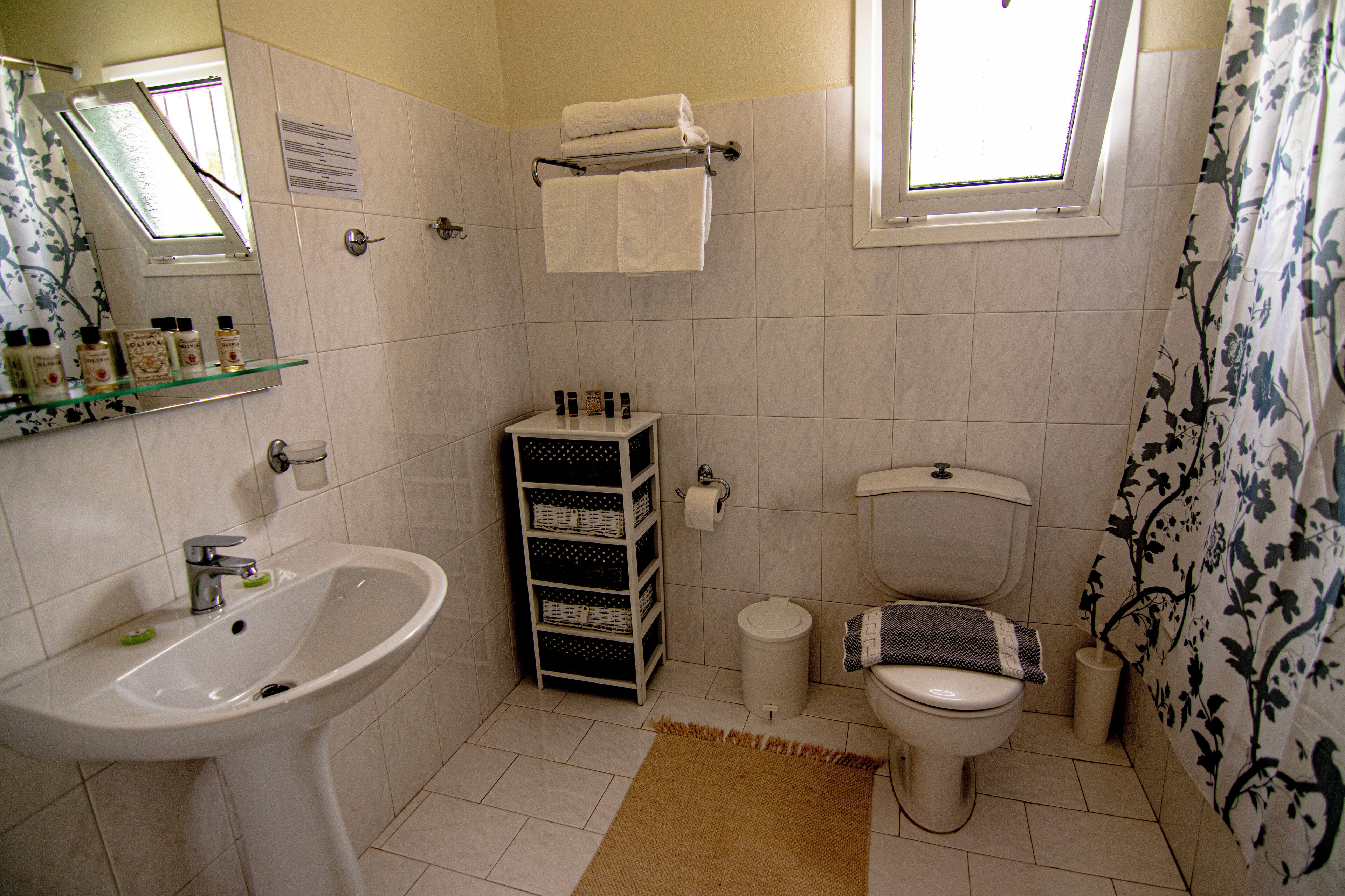 Un baño con lavamanos, inodoro y ventana. Hay toallas colgadas en un perchero y una cortina de ducha.