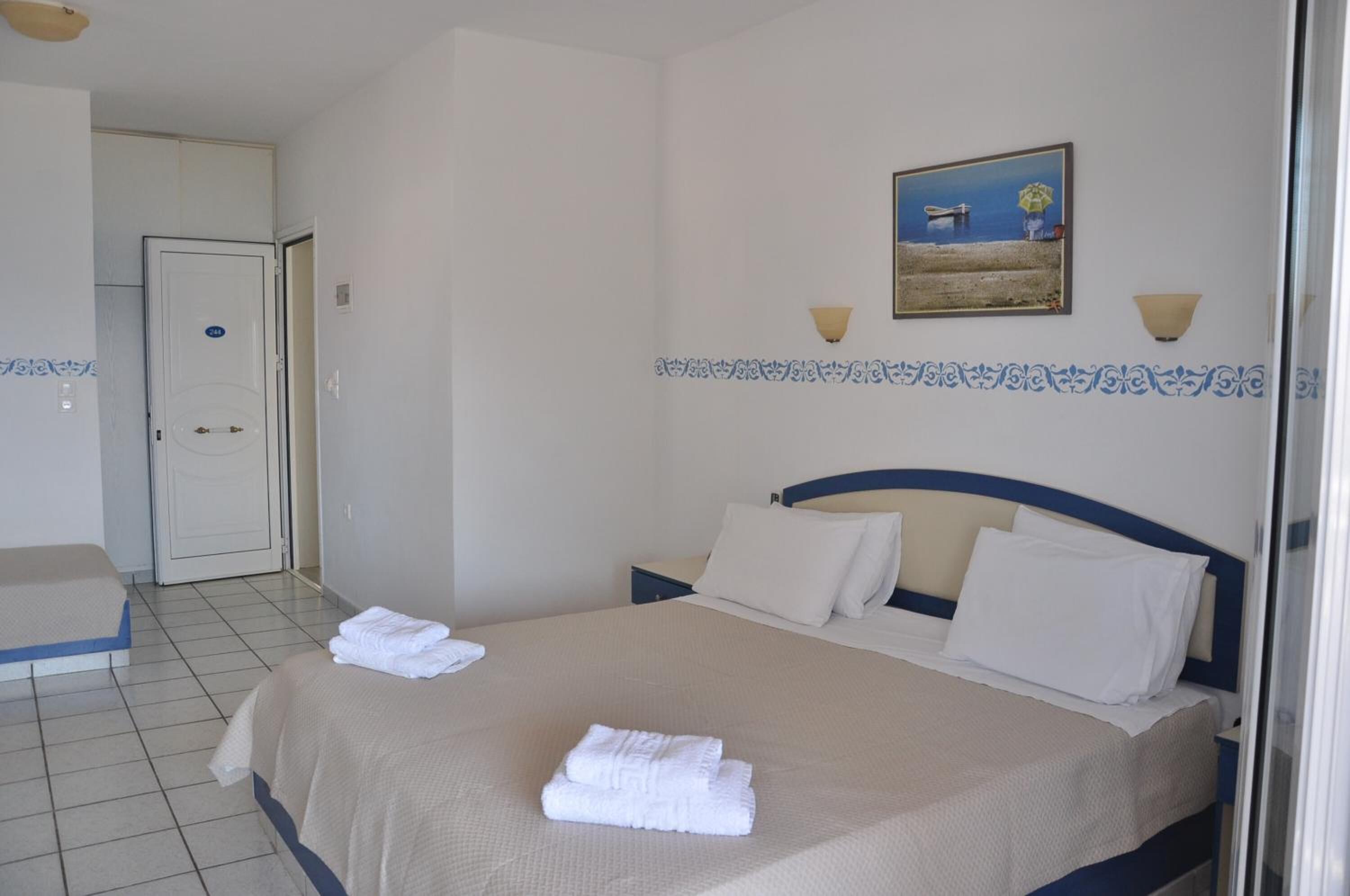 Une chambre d’hôtel avec deux lits, une porte, un tableau et un sol carrelé.