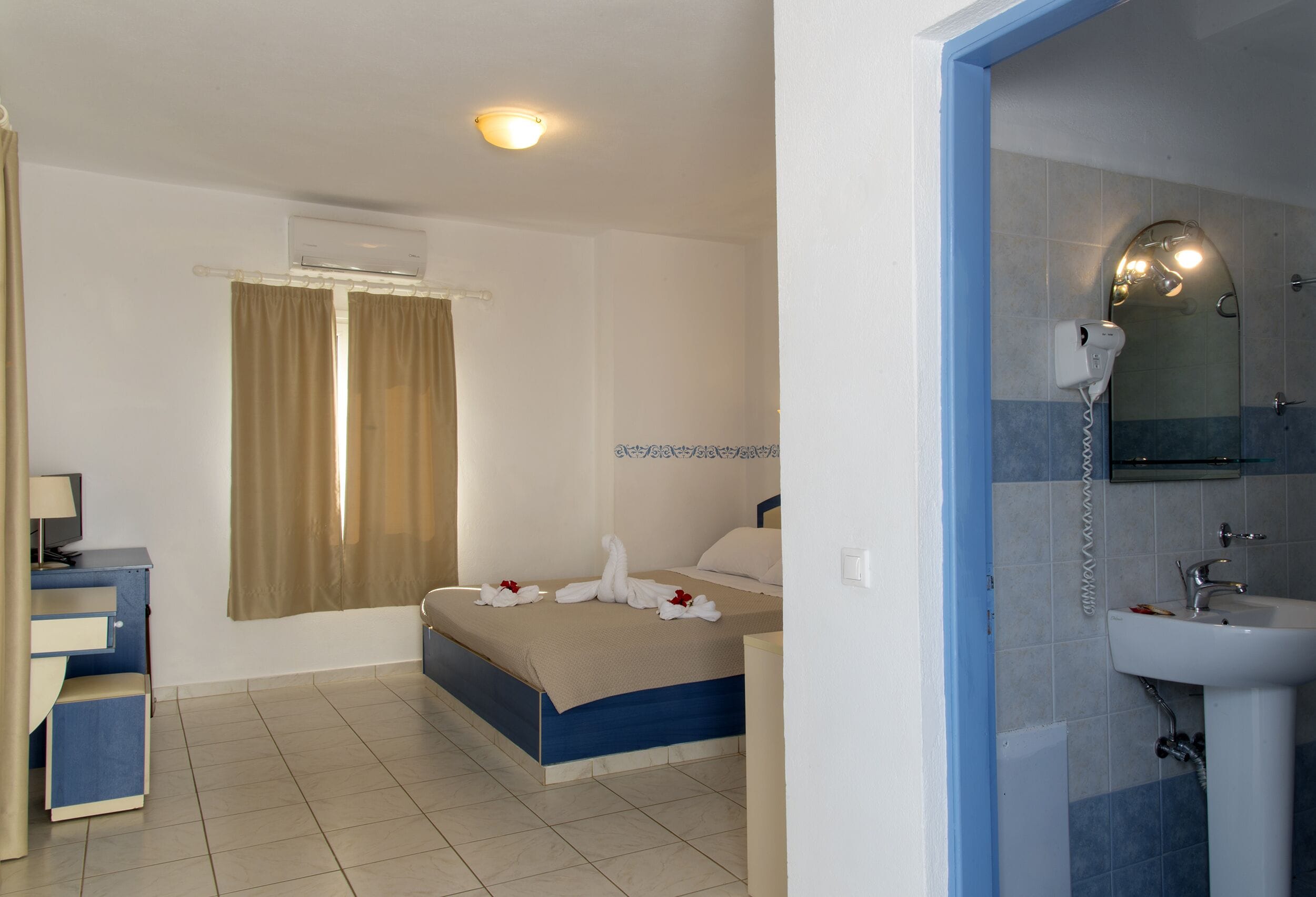 A hotel room with a bed, a desk, a bathroom with a sink and mirror, and a shower area.